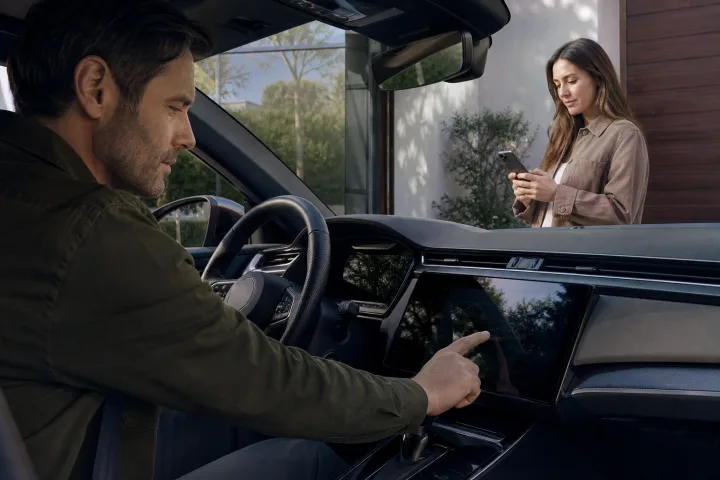 Una persona controlla lo schermo centrale e l’app mobile di un’auto prima di consegnarla a un altro proprietario.