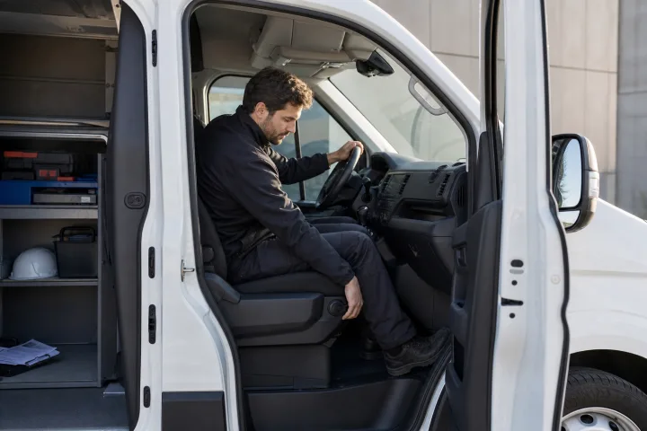 Condutor a ajustar o banco e o volante na cabina de uma carrinha de trabalho estacionada