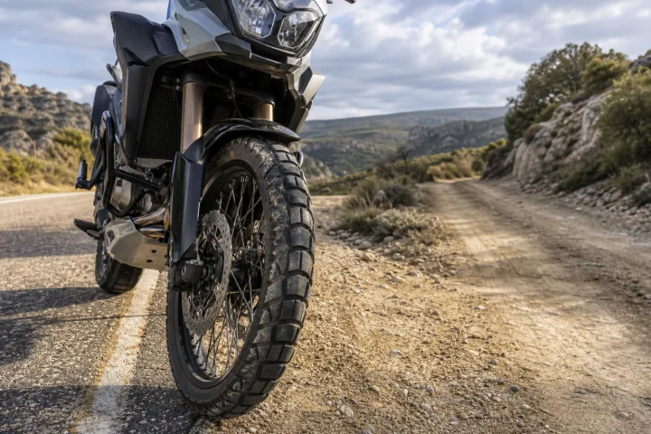 Trail-Motorrad auf Asphalt neben einem Feldweg, mit dem Vorderreifen im Vordergrund.